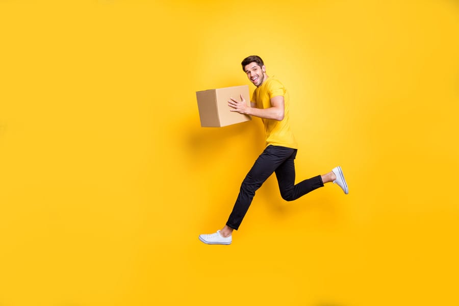 man in yellow top smiling with box in hand against yellow background