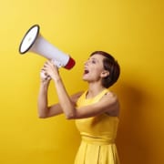 Woman in yellow dress holding megaphone in front of yellow background