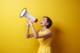 Woman in yellow dress holding megaphone in front of yellow background