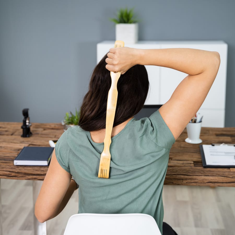 Woman sat at desk scratching her back with back stratcher