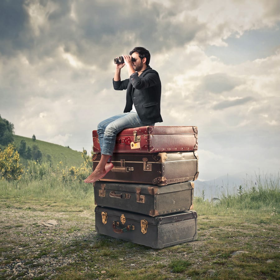 Man sat on pile of suitcases looking through binoculars